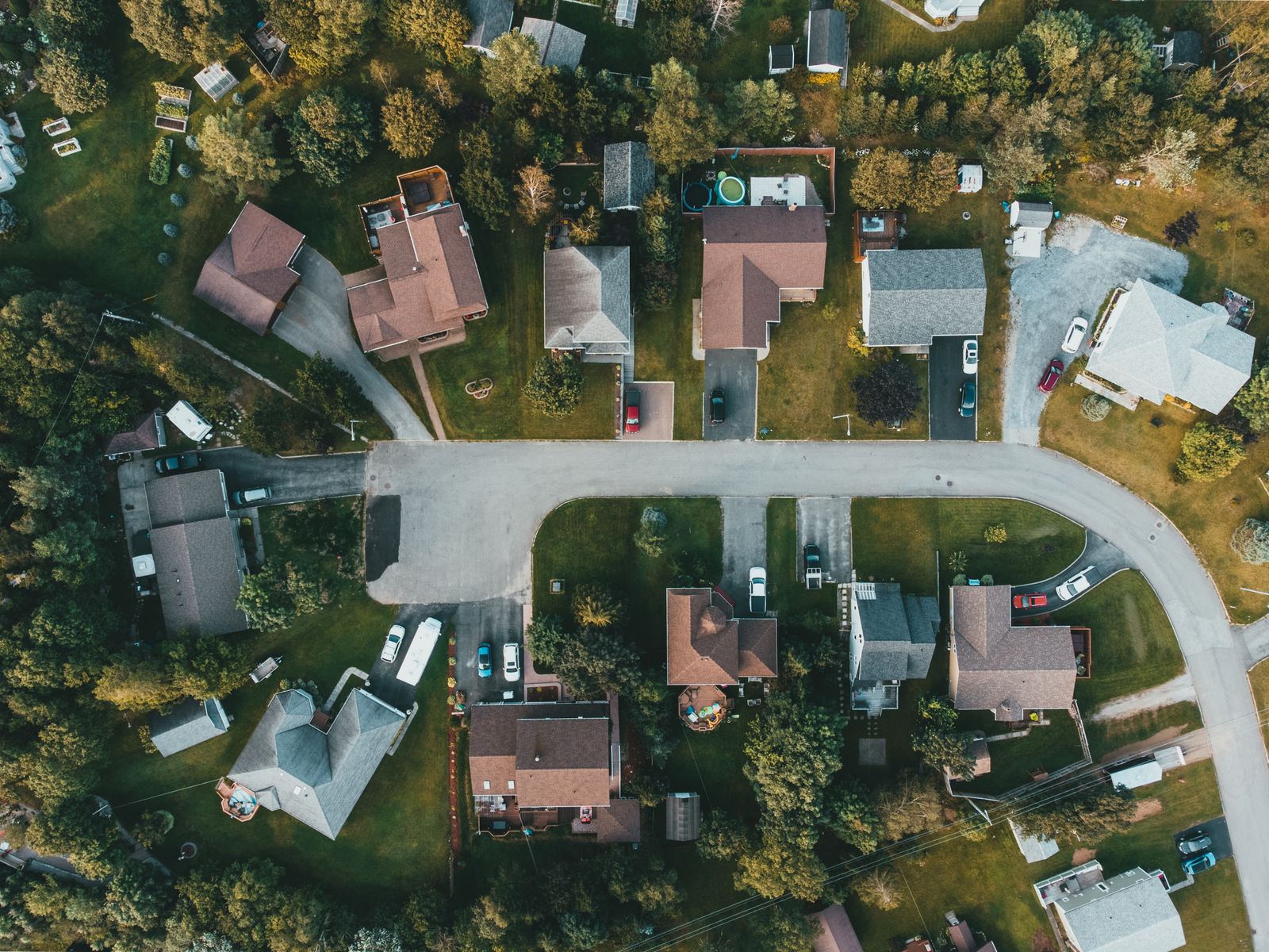 Top-down aerial view of a wooded neighborhood of single-family homes on a curving street